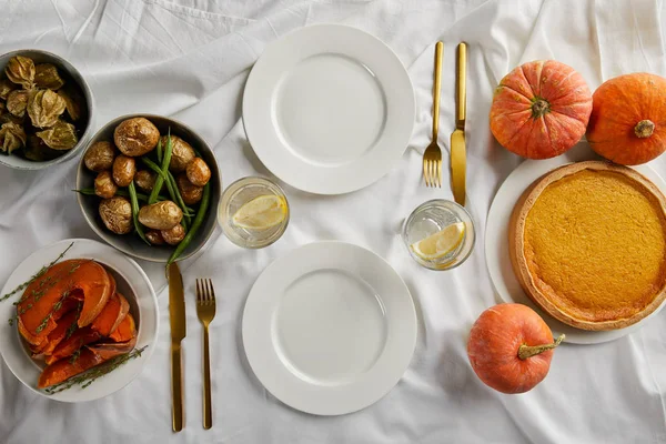 Vista dall'alto della cena servita con torta di zucca, verdure al forno e zucche intere fresche su tovaglia bianca — Foto stock