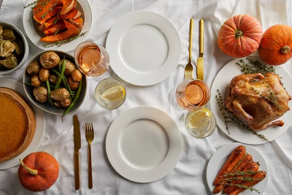 Top view of thanksgiving dinner with grilled turkey, baked vegetables and whole pumpkins on white tablecloth — Stock Photo