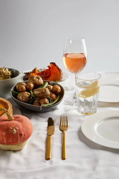 Pommes de terre cuites au four, tranchées et citrouille entière près des verres avec du vin de rose et de l'eau de citron isolés sur gris — Photo de stock