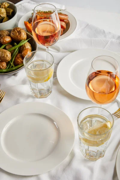 Baked potatoes near glasses with rose wine and lemon water on white tablecloth — Stock Photo