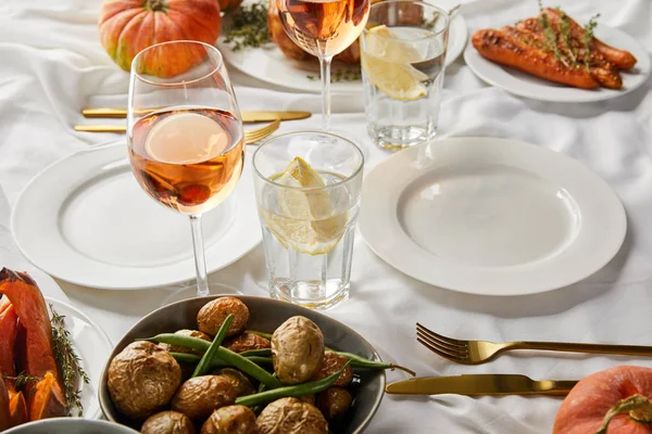 Festive thanksgiving dinner with baked vegetables and glasses with rose wine and lemon water on white tablecloth — Stock Photo