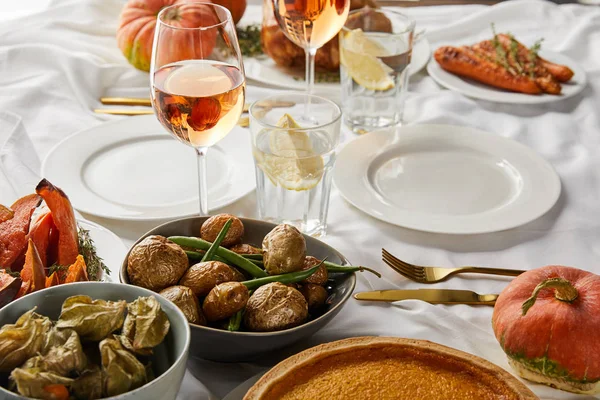Batata assada e physalis perto de copos com vinho rosa e água de limão na toalha de mesa branca — Fotografia de Stock