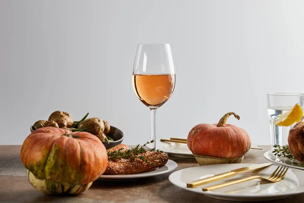 Цілі гарбузи поблизу запеченої картоплі і моркви, і окуляри з трояндовим вином і лимонною водою ізольовані на сірому — стокове фото