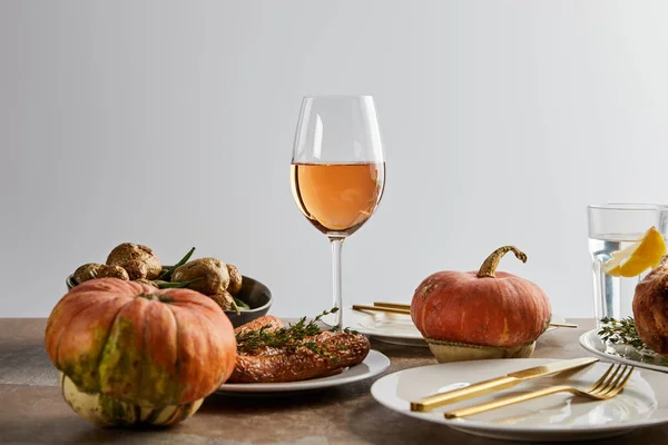 Citrouilles entières près de pommes de terre cuites au four et de carottes, et verres avec vin de rose et eau de citron isolés sur gris — Photo de stock