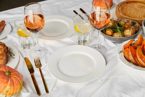 Jantar festivo com legumes sazonais assados perto de copos com vinho rosa e água de limão servido em toalha de mesa branca — Fotografia de Stock