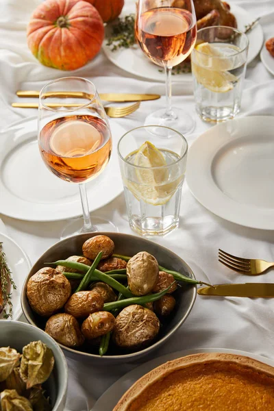 Jantar festivo com legumes sazonais assados perto de copos com vinho rosa e água de limão servido em toalha de mesa branca — Fotografia de Stock