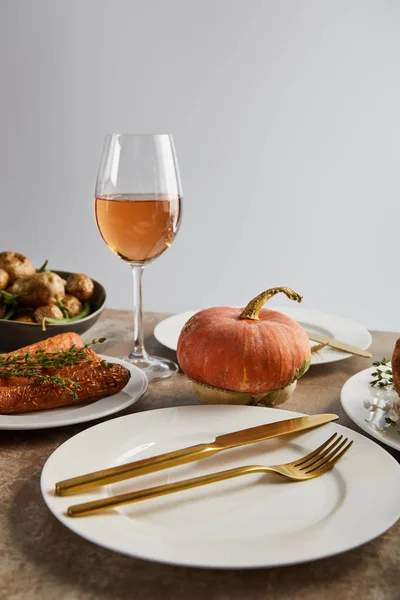 Assiette avec couteau doré et fourchette près de citrouille entière et verre avec vin de rose isolé sur gris — Photo de stock