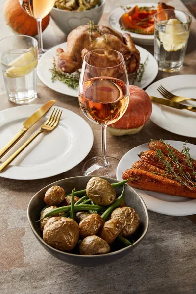 Pommes de terre cuites au four avec des asperges près de la carotte et de la dinde grillées, et des verres avec du vin de rose et de l'eau de citron sur une table en pierre — Photo de stock