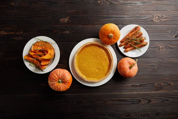 Top view of whole pumpkins, pumpkin pie, baked whole carrot and sliced pumpkin on dark wooden surface — Stock Photo