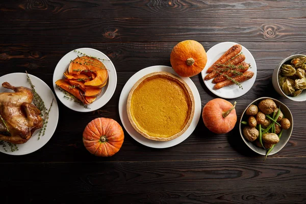 Top view of whole pumpkins, pumpkin pie, baked whole carrot and sliced pumpkin, grilled turkey and potato on dark wooden surface — Stock Photo