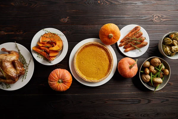 Vista superior de calabazas enteras, pastel de calabaza, zanahoria entera horneada y calabaza en rodajas, pavo a la parrilla y patata en la superficie de madera oscura - foto de stock