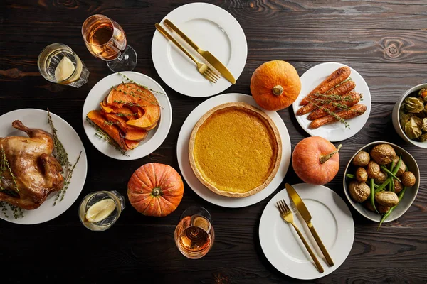 Vista superior de abóboras inteiras, torta de abóbora, legumes assados, peru grelhado e copos com vinho rosa e água de limão na superfície de madeira escura — Fotografia de Stock