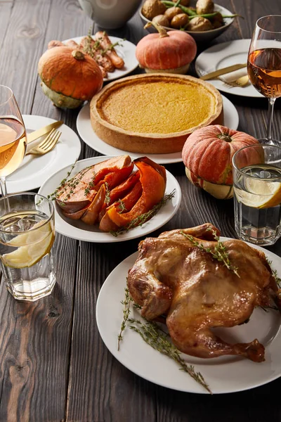 Cena festiva con pavo a la parrilla, verduras horneadas, pastel de calabaza y vasos con vino de rosas y agua de limón en la mesa de madera oscura - foto de stock