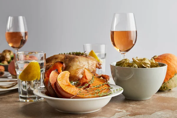 Праздничный день благодарения с запечённой тыквой, индейкой на гриле и стаканами с розовым вином и лимонной водой, изолированными на сером — стоковое фото