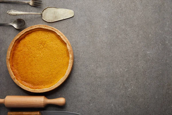 Vue du dessus du délicieux gâteau à la citrouille près des couverts et du rouleau à pâtisserie sur la surface en pierre grise — Photo de stock