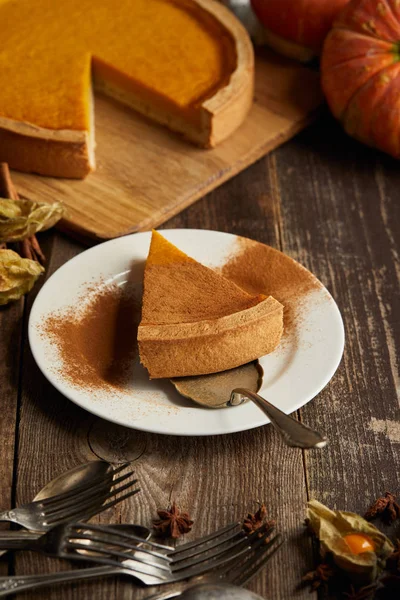 Délicieuse tarte à la citrouille avec de la poudre de cannelle près des couverts sur une surface en bois sombre — Photo de stock