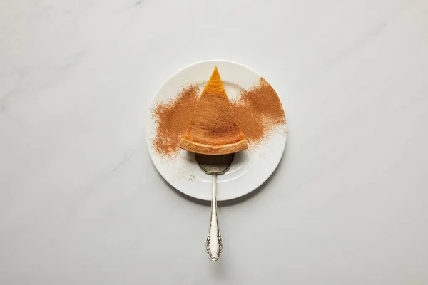 Вид сверху на тыквенный пирог с порошком корицы на тарелке с лопаткой на поверхности белого мрамора — стоковое фото