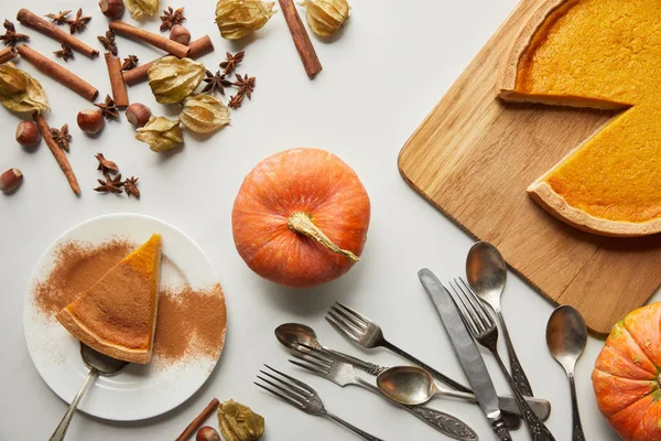 Top view of delicious pumpkin pie near whole pumpkin, spices and cutlery on white marble surface — Stock Photo