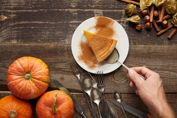 Top view of male hand with spatula near delicious pumpkin pie wit cinnamon powder on dark wooden surface — Stock Photo
