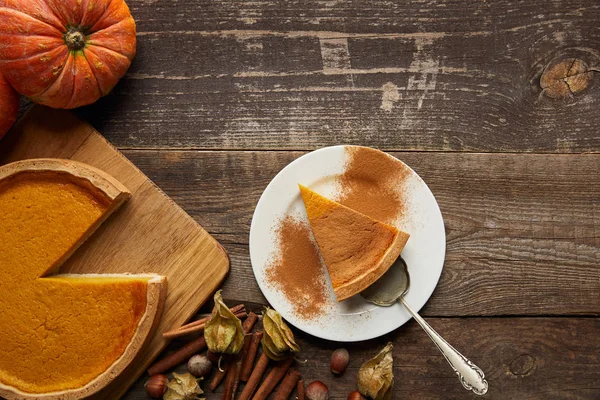 Top view of pumpkin pie with cinnamon powder near whole pumpkin and spices on dark wooden surface — Stock Photo