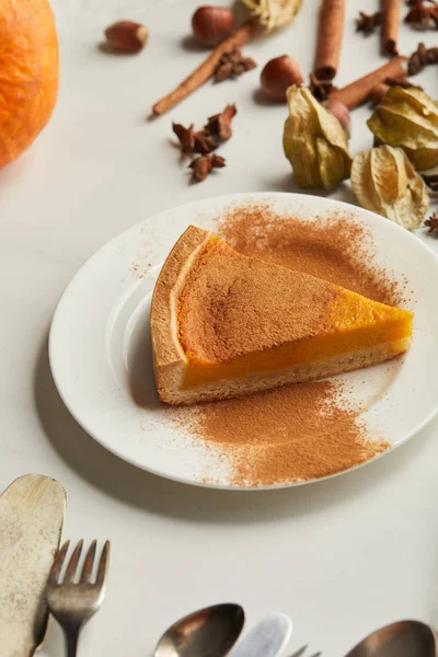 Delicious pumpkin pie with cinnamon powder near cutlery and spices on white marble surface — Stock Photo