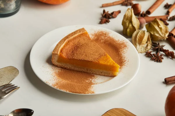 Tasty pumpkin pie with cinnamon powder near cutlery and spices on white marble surface — Stock Photo