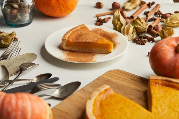 Messa a fuoco selettiva di deliziosa torta di zucca vicino a posate e spezie sulla superficie di marmo bianco — Foto stock