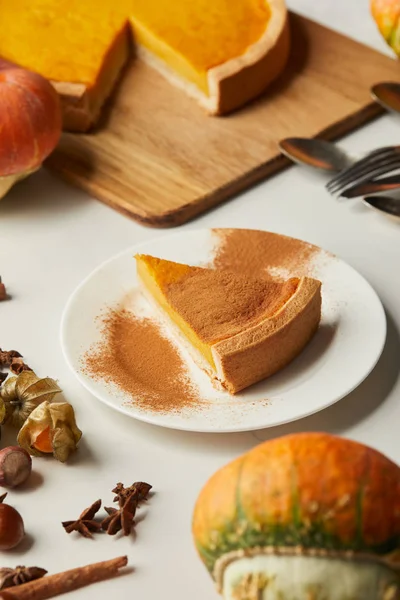 Foco selectivo de pastel de calabaza sabrosa cerca de calabaza entera y especias en la superficie blanca - foto de stock