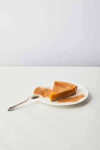 Delicious pumpkin pie with cinnamon powder on plate near spoon of white marble table isolated on grey — Stock Photo