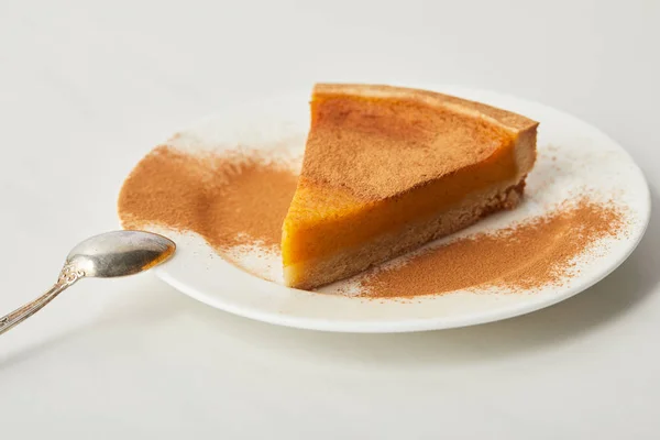 Tasty pumpkin pie with cinnamon powder on plate near spoon of white marble table — Stock Photo