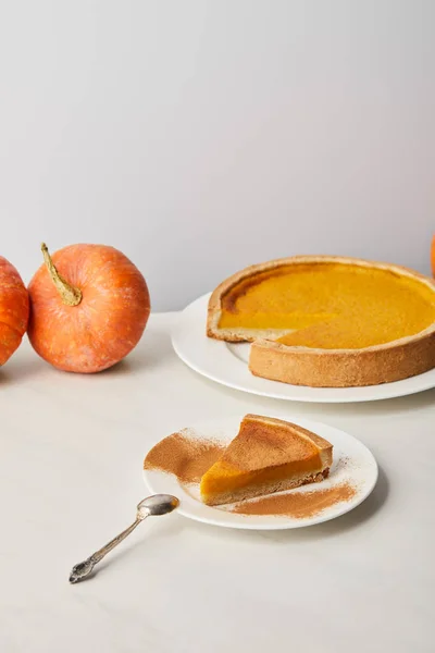 Tasty pumpkin pie with cinnamon powder near whole ripe pumpkins on white marble surface isolated on grey — Stock Photo
