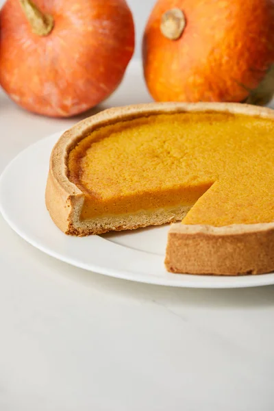 Selective focus of delicious pumpkin pie near whole ripe pumpkins on white surface — Stock Photo