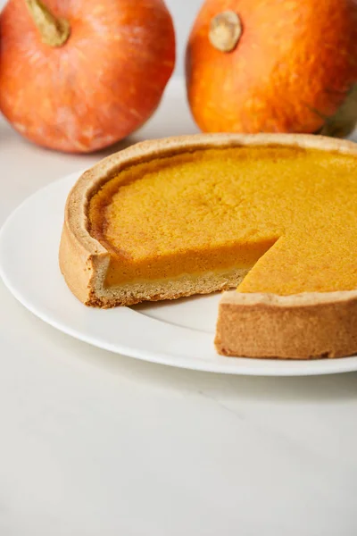 Selektiver Fokus von leckerem Kürbiskuchen in der Nähe ganzer reifer Kürbisse auf weißer Oberfläche — Stockfoto