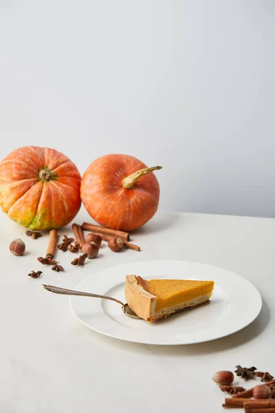 Leckere Kürbiskuchen in der Nähe, während Kürbisse und Gewürze isoliert auf grau mit Kopierraum — Stockfoto