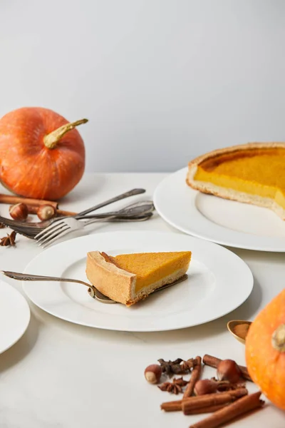 White plates with tasty pumpkin pie near cutlery and spices isolated on grey — Stock Photo