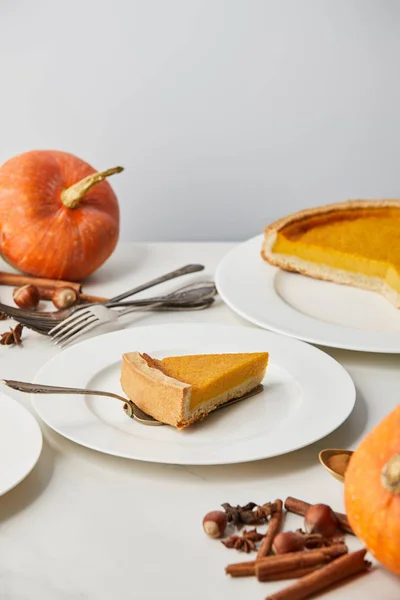 Assiettes blanches avec tarte à la citrouille savoureuse près des couverts et des épices isolées sur gris — Photo de stock