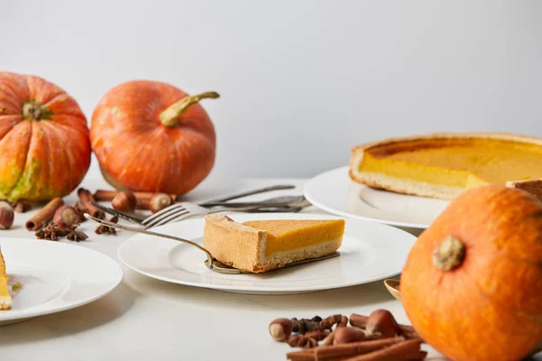 Assiettes blanches avec tarte à la citrouille savoureuse près de citrouilles entières, couverts et épices isolés sur gris — Photo de stock