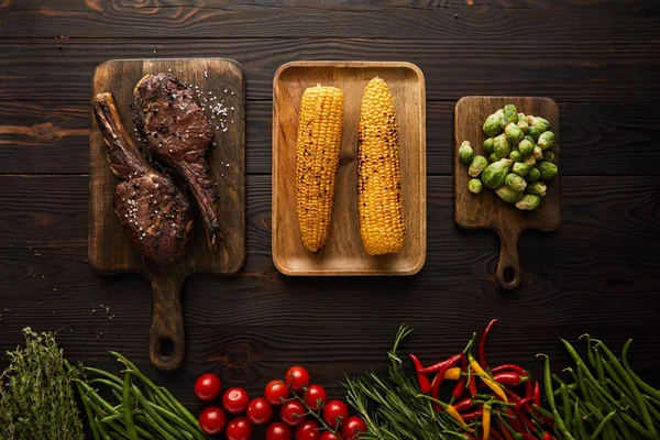 Blick von oben auf Fleisch, Mais, Chilischoten, Kirschtomaten, grüne Erbsen, Grün, Rosenkohl auf Schneidebrett — Stockfoto