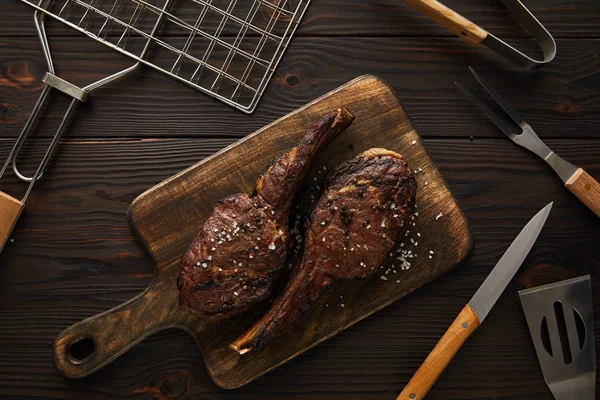 Верхний вид мяса на режущей доске и гриль инструменты — стоковое фото