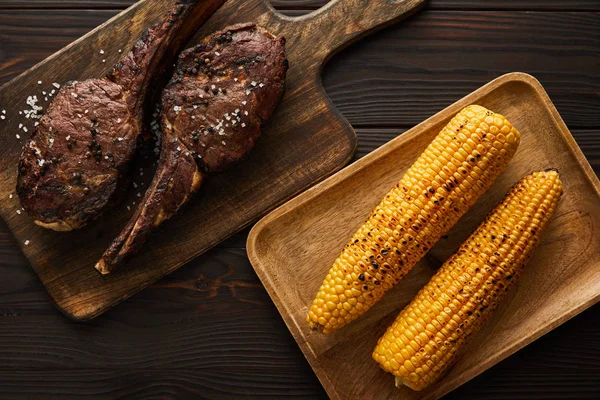 Top view of tasty meat and corn on cutting boards — Stock Photo