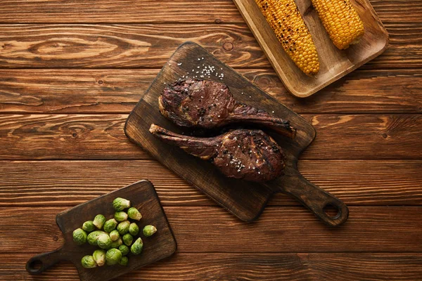 Vista superior de brotes de carne, maíz y Bruselas en tablas de cortar - foto de stock