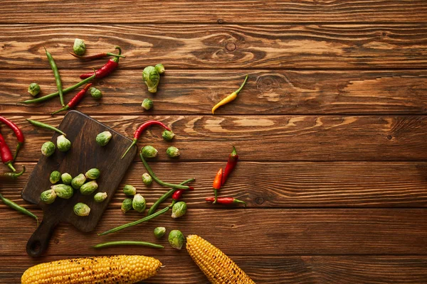 Vue du dessus de maïs, piments, pois verts, choux de Bruxelles sur planche à découper — Photo de stock