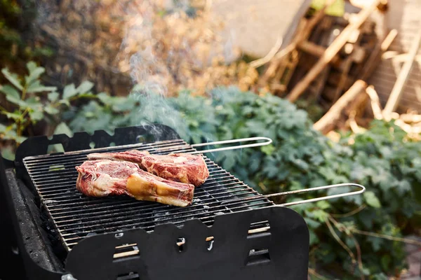 Raw meat grilling on barbecue grid and coal pieces outside — Stock Photo