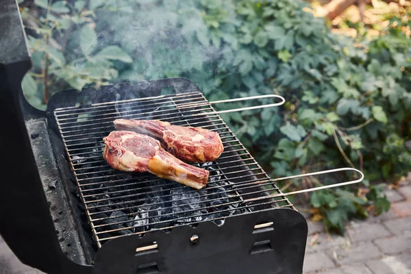 Raw meat grilling on barbecue grid and coal pieces outside — Stock Photo