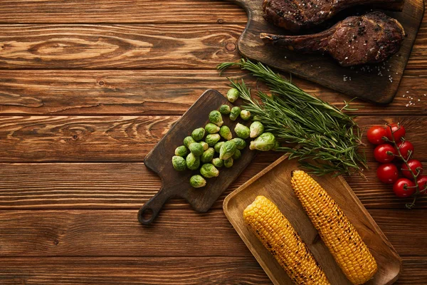 Вид на мясо, кукурузу, помидоры черри, зелень, брюссельскую капусту на разделочной доске — стоковое фото