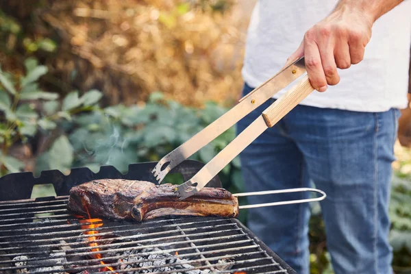 Vista cortada do homem com pinças grelhando carne na grelha de churrasco — Fotografia de Stock