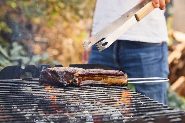 Vista cortada do homem com pinças grelhando carne na grelha de churrasco — Fotografia de Stock