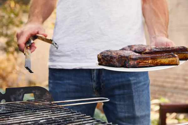 Vista recortada del hombre con pinzas que sostienen la carne en el plato - foto de stock