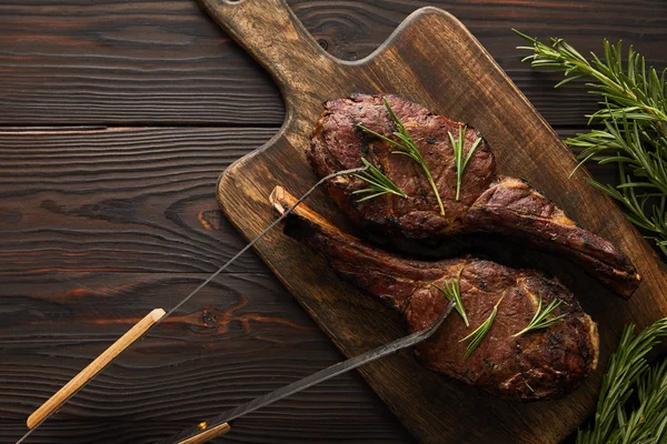 Vista superior de carne saborosa com vegetação na tábua de corte e pinças — Fotografia de Stock