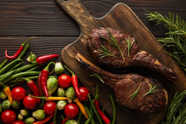 Top view of meat on cutting board, chili peppers, cherry tomatoes, green peas, greenery, brussels sprouts — Stock Photo